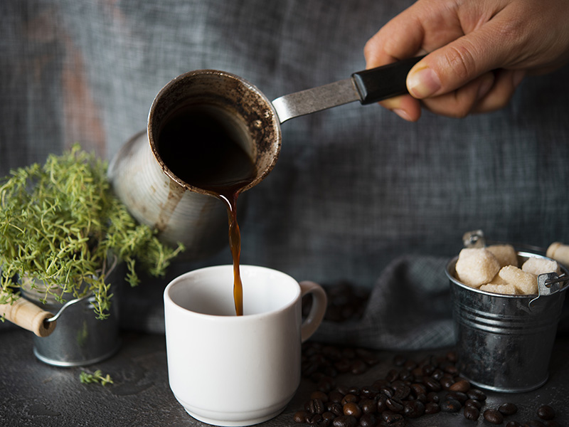 turkish coffee beeing poured into a coffee cup from an vintage coffee kettle